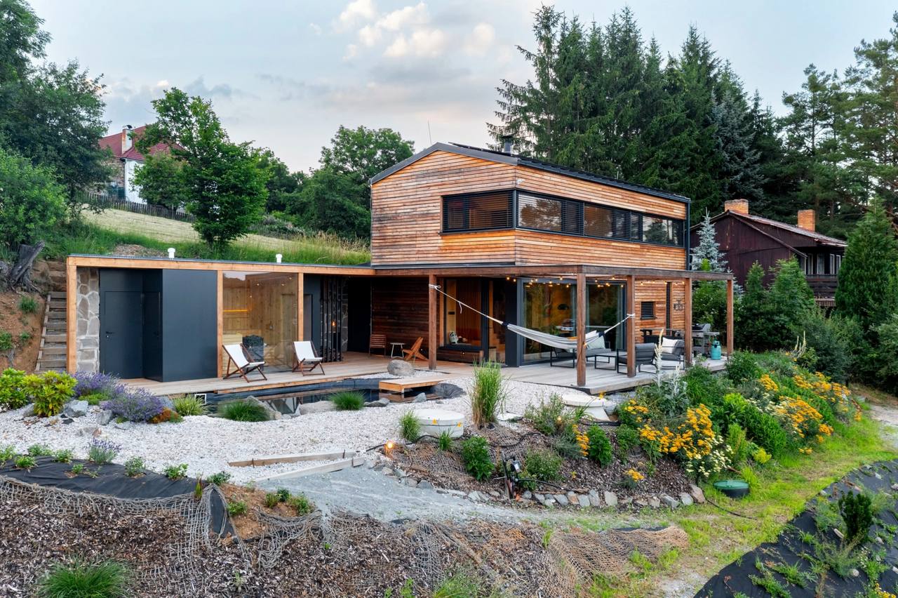 The house seen from the garden: cedar cladding, a covered terrace with a hammock, and the pond planting in front