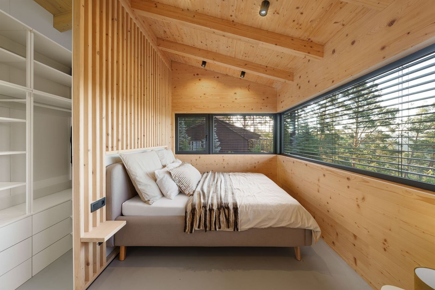 A bedroom with a panoramic corner window looking over the trees